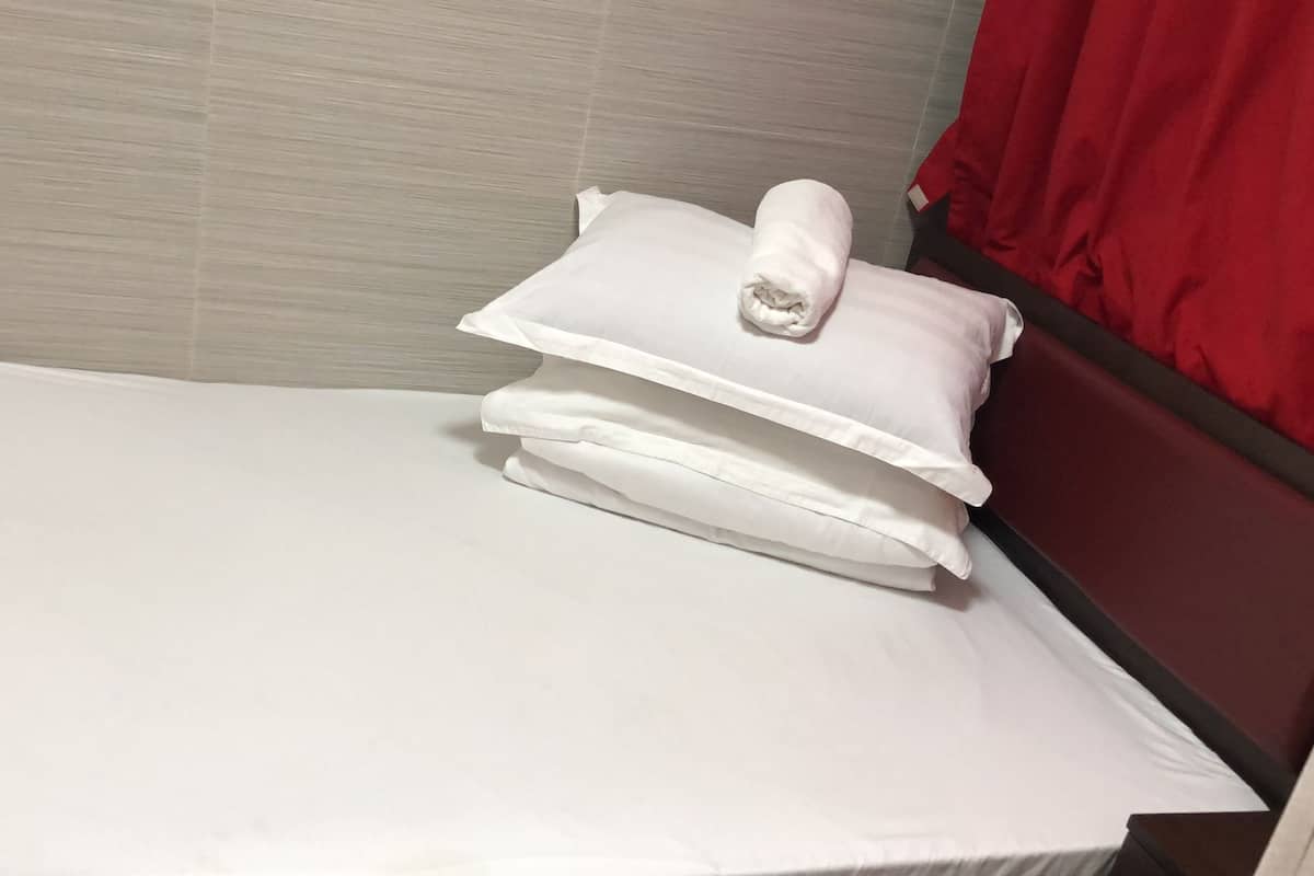 A neatly made bed with white linens and pillows, a wooden headboard, and a red curtain.