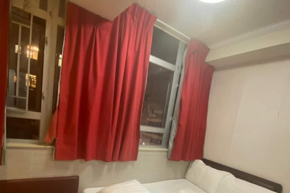 A hotel room with a bed, a nightstand, a window with red curtains, and a staircase.
