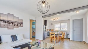 A modern apartment with a living room, dining area, and kitchen. There is a glass coffee table in the living room, a dining table with chairs, and a kitchen with a stove and cabinets. - Janomaine by Interhome (Cabourg)