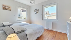 A bedroom with two beds, large windows, a radiator, and a hanging light fixture. - Janomaine by Interhome (Cabourg)