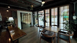Un restaurant avec des tables et des chaises en bois, un mur en briques et de grandes fenêtres équipées de stores.