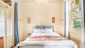 Une chambre à coucher avec un lit, deux tables de chevet, une fenêtre avec des rideaux et une porte.