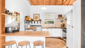 A compact kitchen with white cabinetry, a wooden countertop, and a bar area with stools. - Cooee Cottage @ Blackheath (Blackheath)