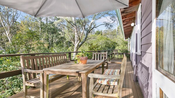 Une terrasse extérieure avec une table et des chaises en bois, une plante en pot et un grand parasol.