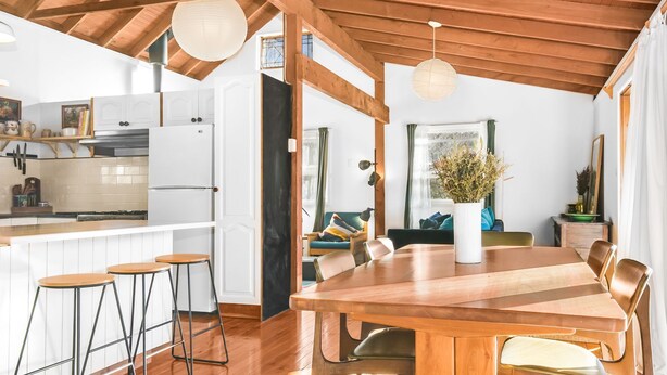 A spacious kitchen with white cabinets, a wooden dining table, and bar stools. - Cooee Cottage @ Blackheath (Blackheath)