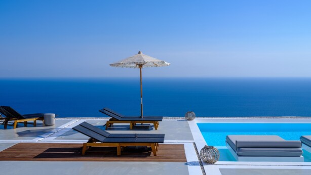 A poolside area with lounge chairs, a pool, and a view of the ocean.