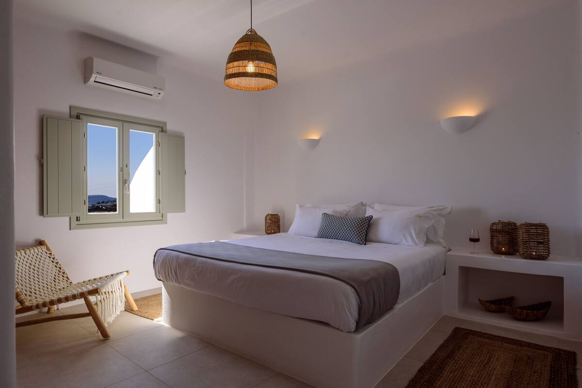 Un dormitorio con cama, una silla, una estantería con adornos y una ventana con contraventanas.