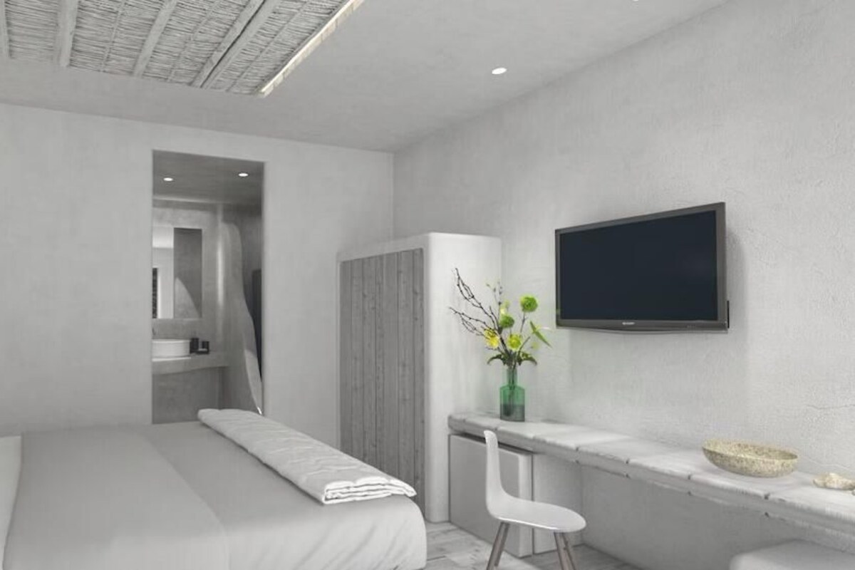 Habitació d'hotel moderna amb un llit, escriptori, cadira, televisió i una taula petita amb un bol.