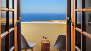 An open balcony with two chairs and a small wooden table, overlooking a clear blue sea and a distant coastline.