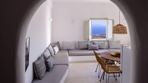 A modern living room with a sofa, dining table, and chairs, a large window with a view, and a hanging light fixture.