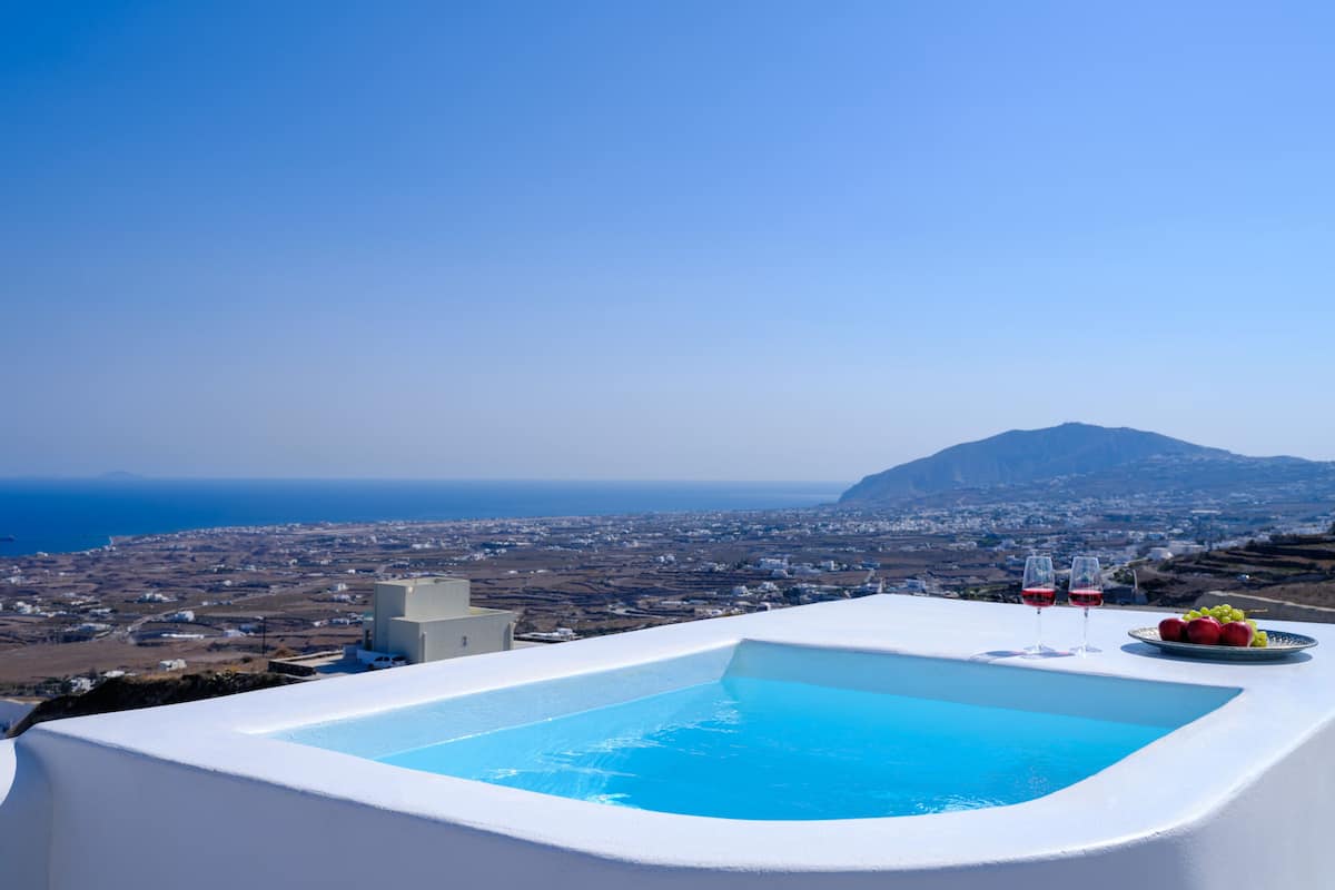 Una piscina infinita blanca con un cielo azul despejado y vista a un pueblo costero.