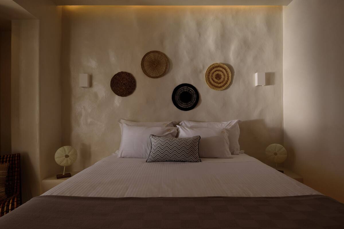 Un dormitorio con cama, almohadas, una silla y adornos en la pared.