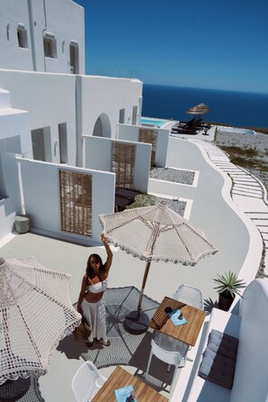 A terrace with white architecture, outdoor seating, and a view of the sea. - Terra Blanca Suites (Santorini)