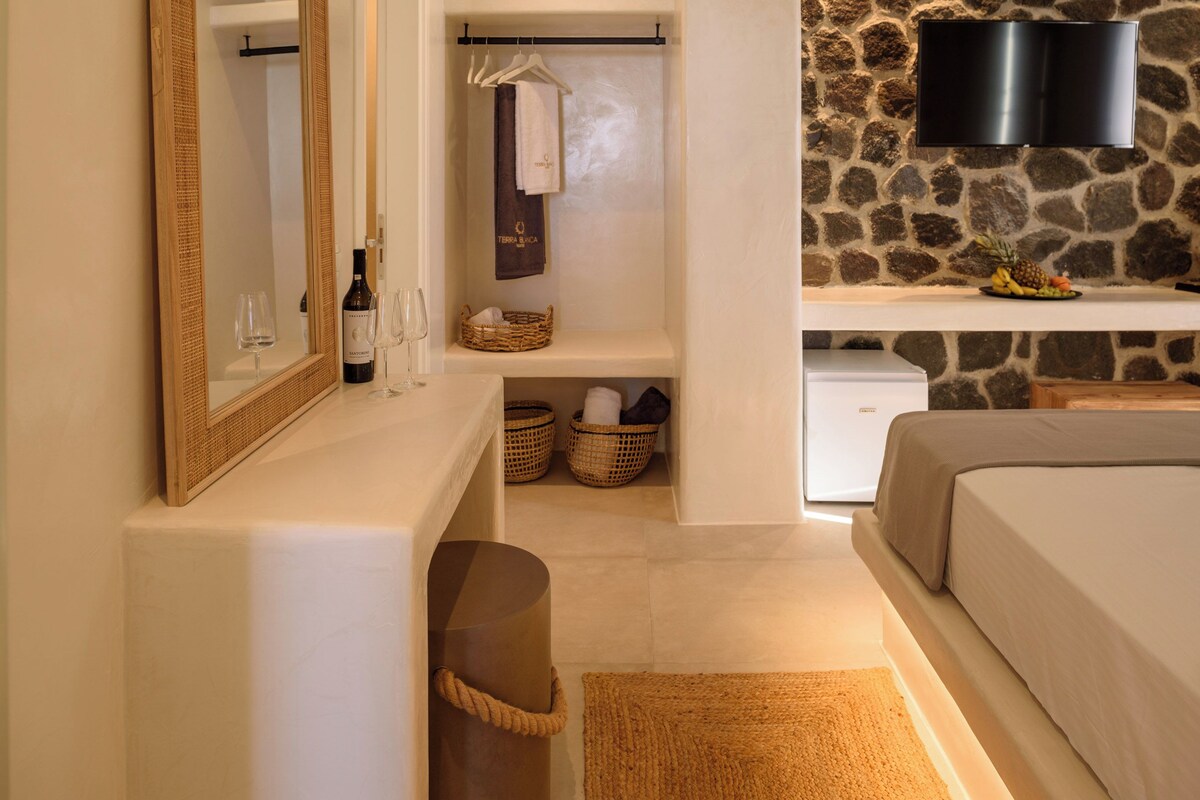 A modern bedroom with a stone wall, a flat-screen TV, a bed, a bedside table, a mirror, and a small seating area.