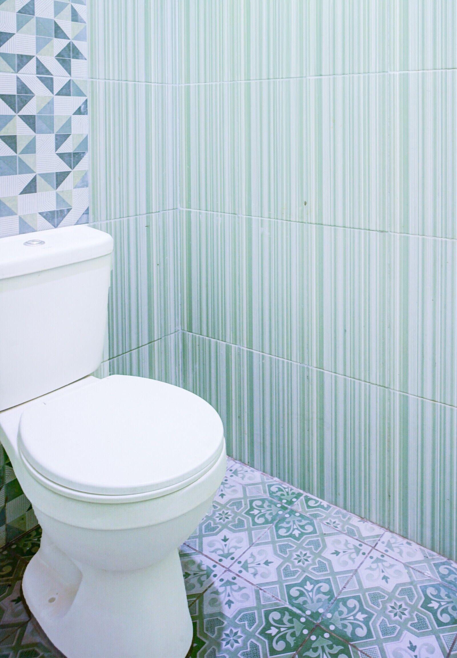 Une salle de bain avec des toilettes, des murs à rayures vertes et des carreaux de sol à motifs.