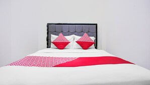 Ein Bett mit grau gepolstertem Kopfteil, zwei roten Kissen und einer Bettdecke mit weiß-rotem Muster.