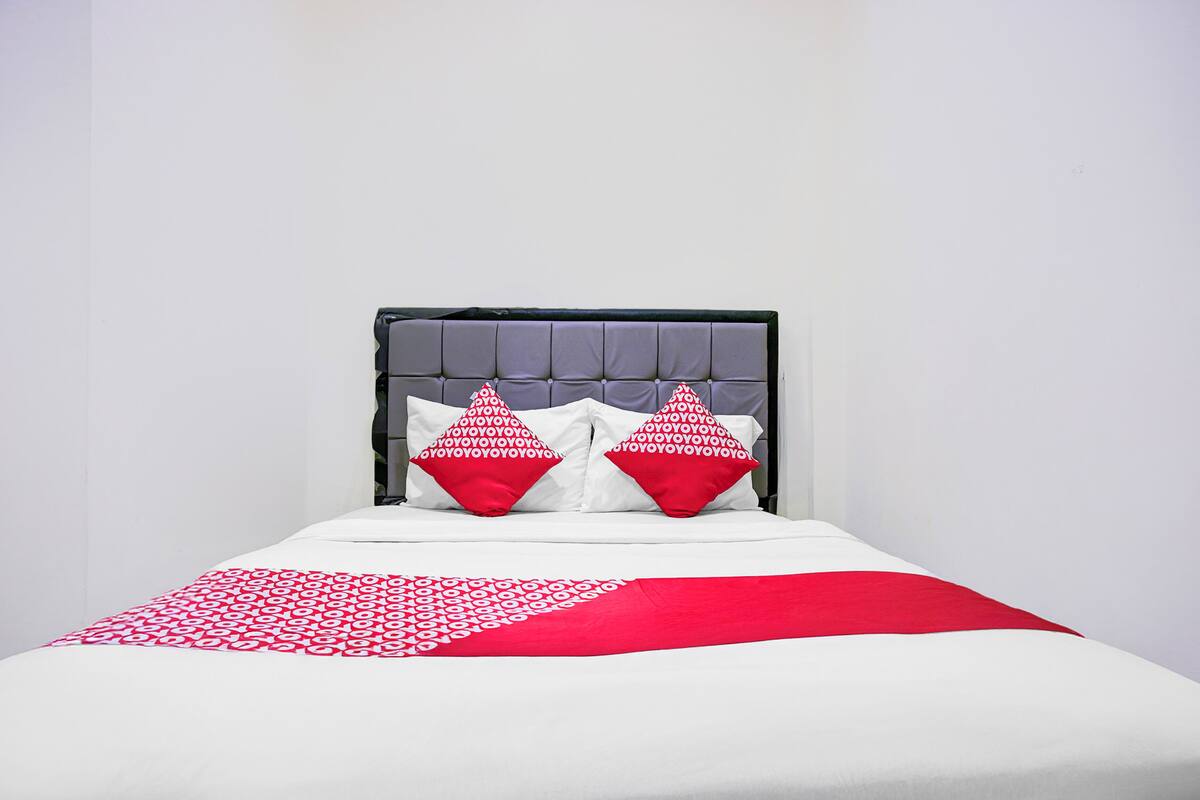 A bed with a grey upholstered headboard, two red pillows, and a white and red patterned bedspread.