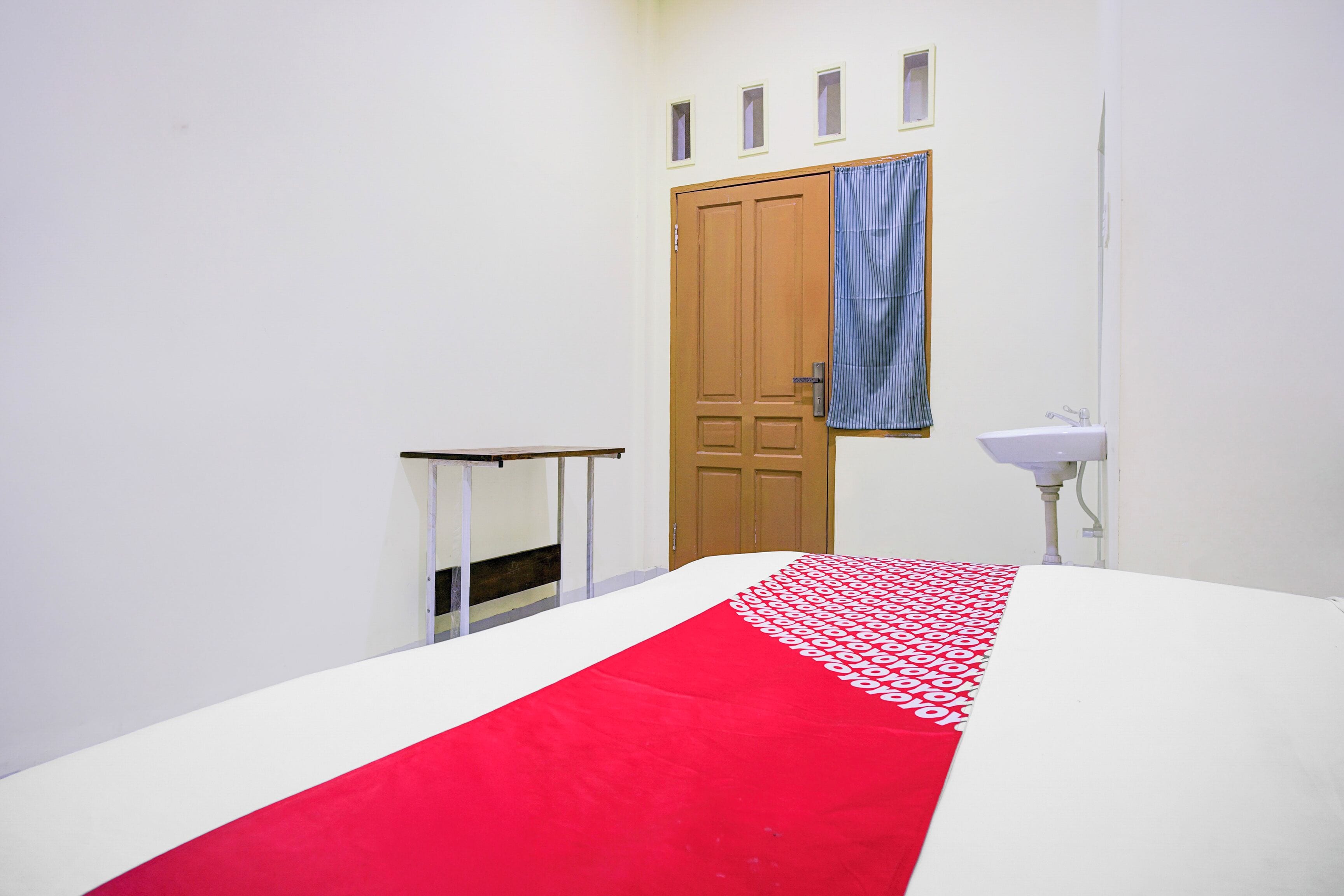 Habitación de hotel con cama, una puerta de madera, una ventana con cortina y una mesita de noche con espejo.