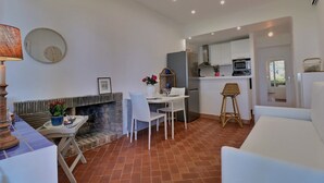 A modern kitchen with white cabinets, a microwave, and a built-in oven. There is a dining area with a white table and chairs, and a small seating area with a white sofa. - Apartment, 1 bedroom, Shared pool, Private beach, Mediterranean garden (La Croix-Valmer)