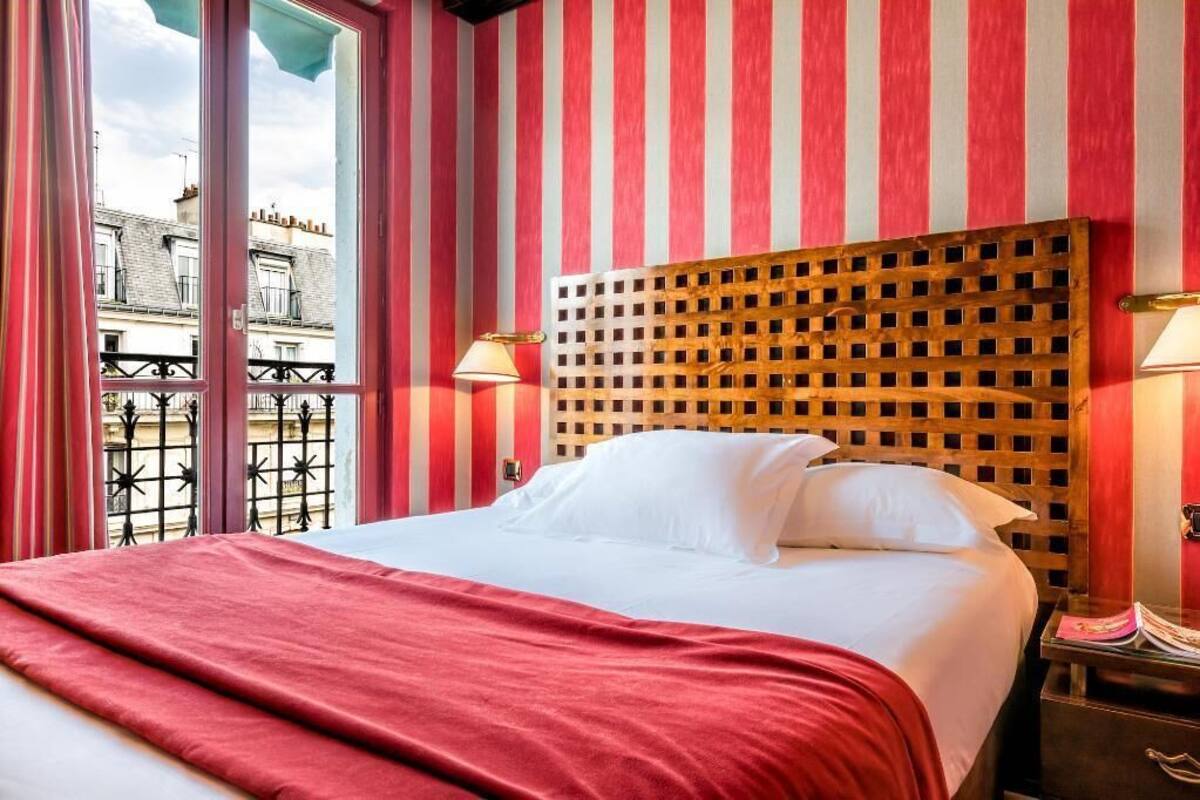 A hotel room with a bed, striped walls, a wooden headboard, and a balcony view.