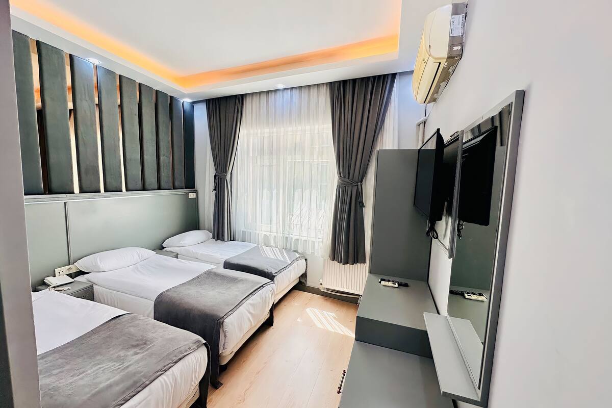A hotel room with two beds, a TV, a mirror, and a window with curtains.
