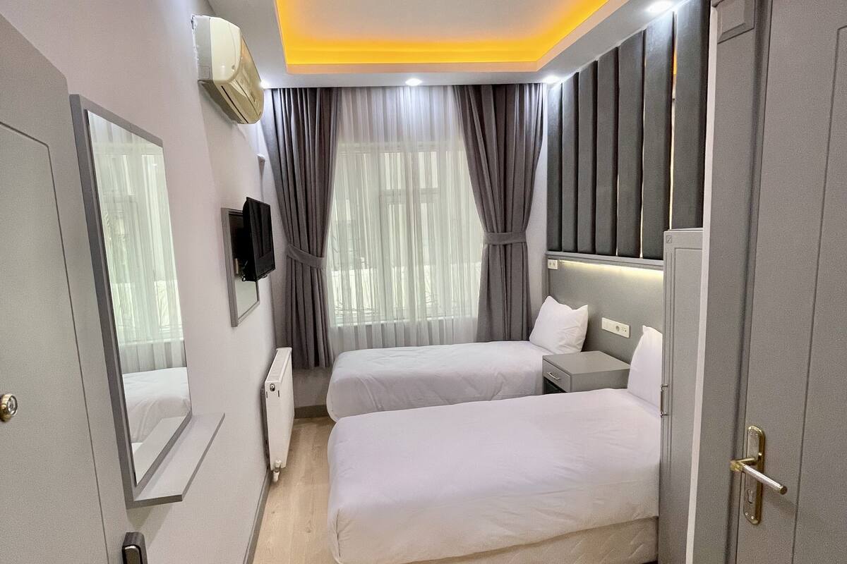 A modern hotel room with two single beds, a large mirror, an air conditioning unit, and a wardrobe.