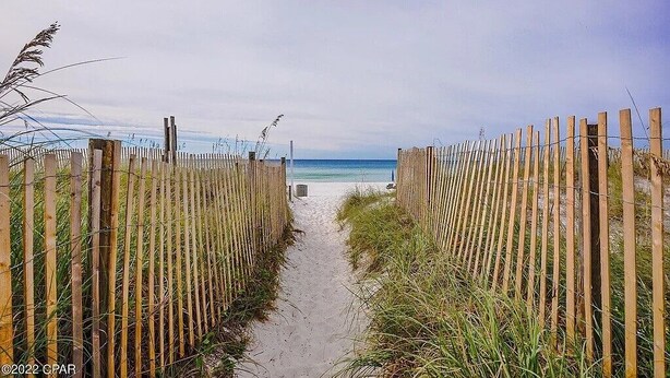 Ein Sandweg am Strand, gesäumt von Holzzäunen, der zum Meer führt.