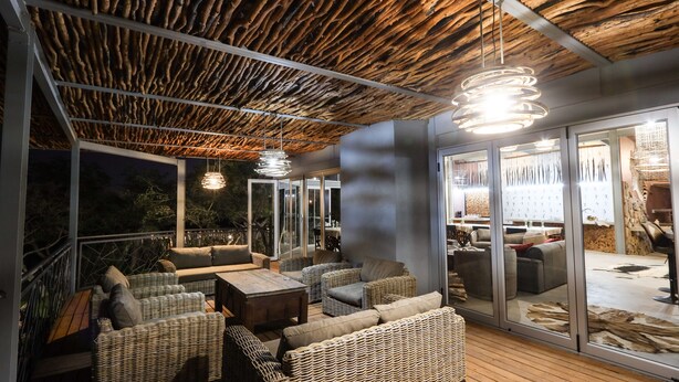 An outdoor seating area with wicker furniture, glass doors, and hanging pendant lights. - Mountain Peak Game Lodge Namibia (Outjo)