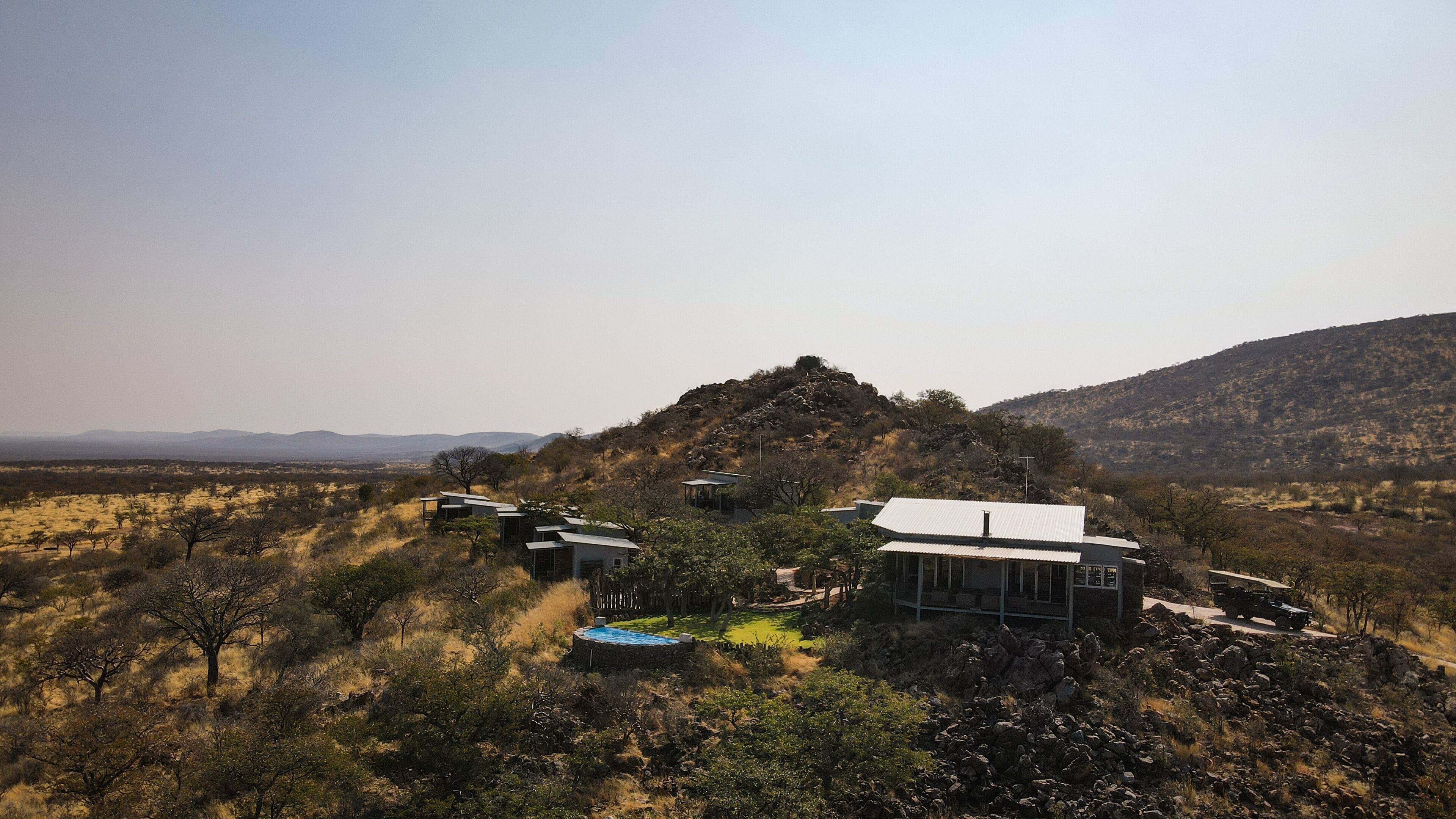 Une villa moderne et isolée, dotée d’une piscine et de nombreuses pièces, entourée d’un paysage naturel et bordée de montagnes lointaines.