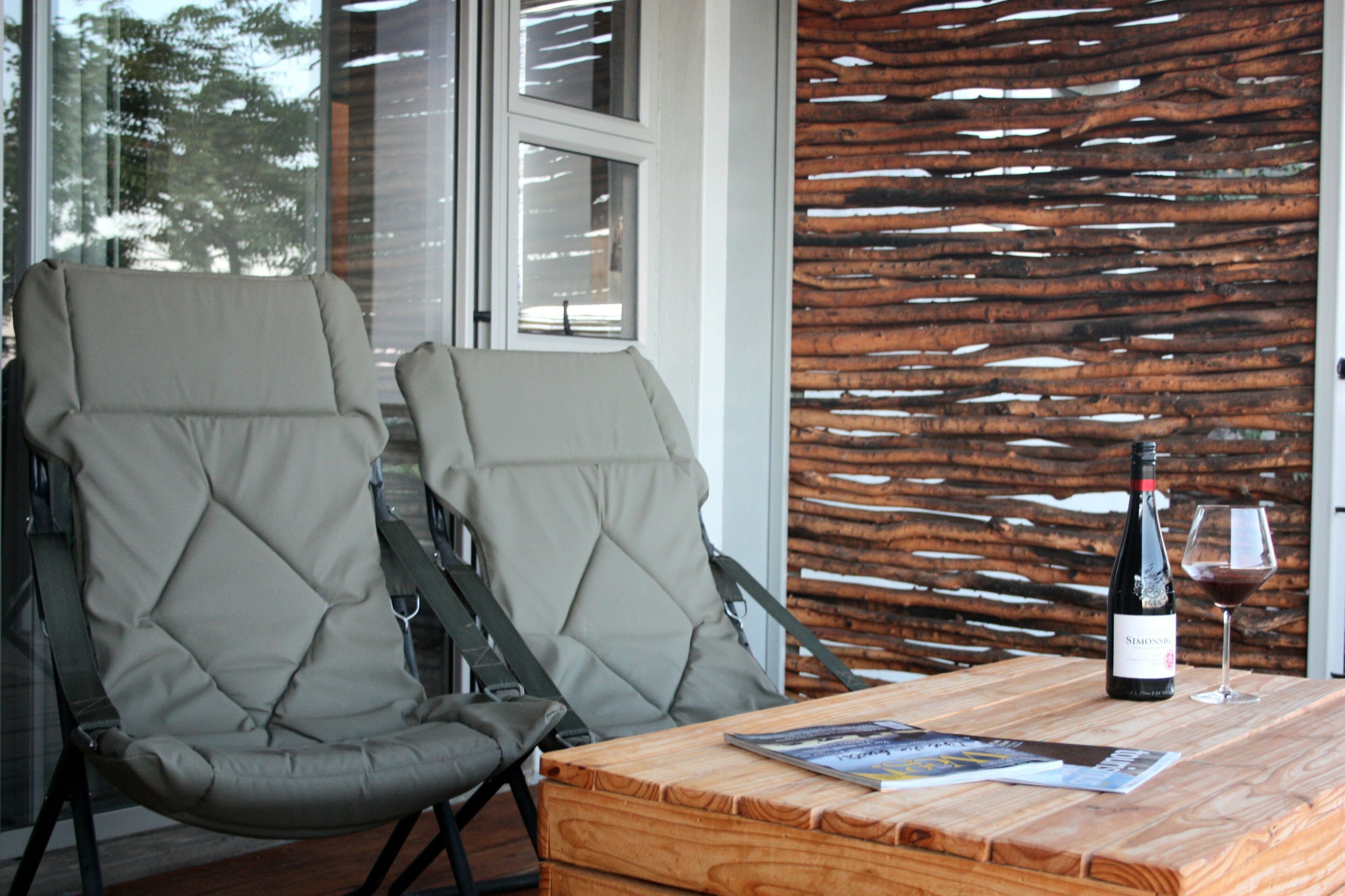 Dos sillones cómodos, una mesa de madera con una botella de vino y una copa, y una pared de madera con un diseño único.