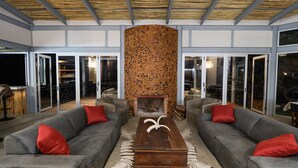 A modern outdoor living area with two grey sofas, a wooden coffee table, and a central decorative wall. - Mountain Peak Game Lodge Namibia (Outjo)
