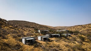 A series of modern, minimalist cabins in a dry, hilly landscape. - Mountain Peak Game Lodge Namibia (Outjo)