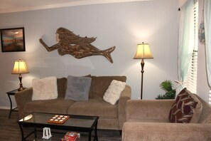 A living room with a brown sofa, two side tables with lamps, a coffee table with a board game, and a decorative piece on the wall. - Stay Salty - Kontiki (Rockport)
