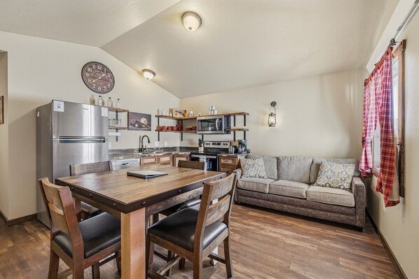 A compact kitchen with a dining table, chairs, a sofa, and a clock on the wall.