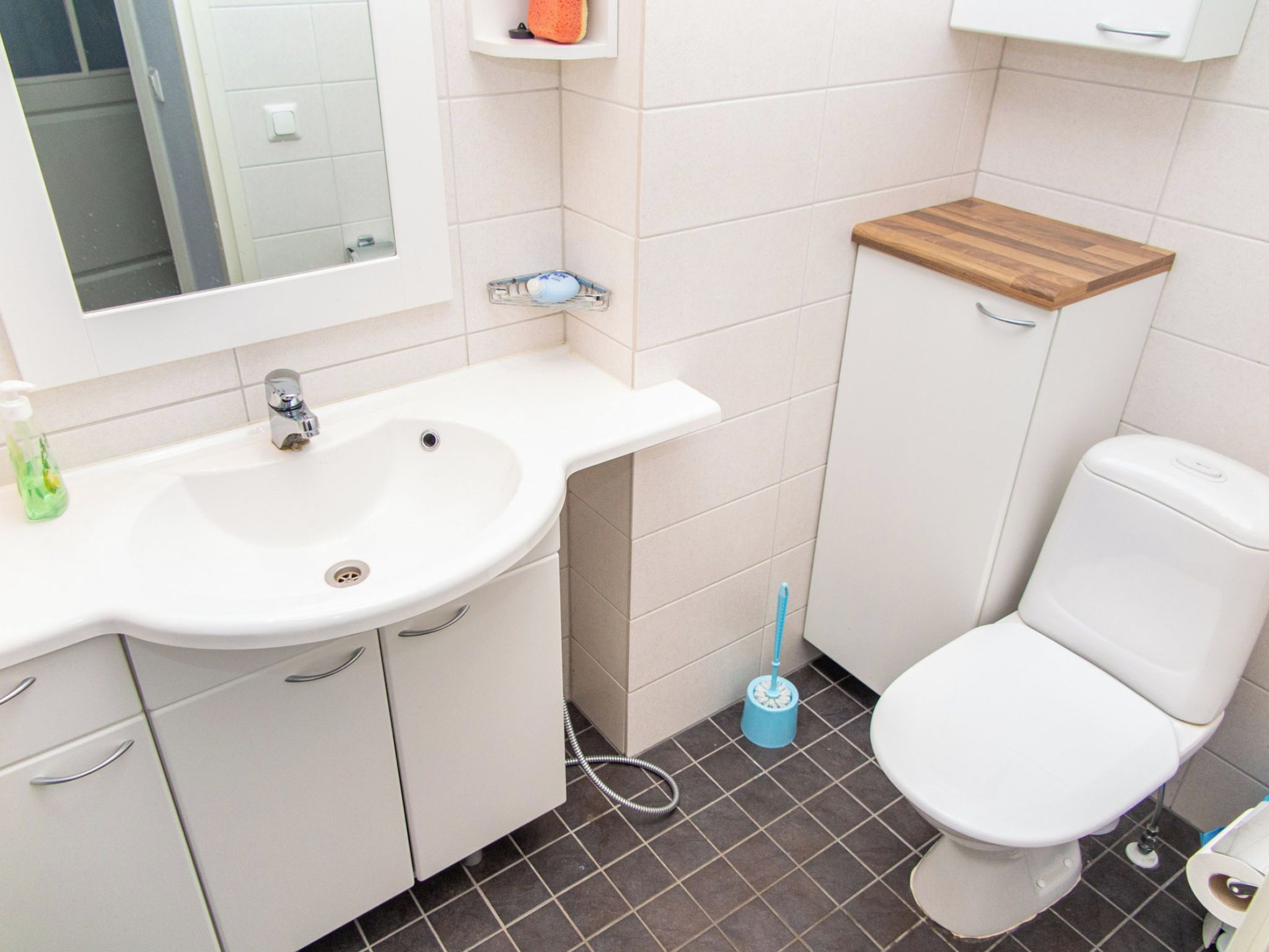 Une salle de bain avec un lavabo blanc, un miroir, des toilettes et une brosse de nettoyage bleue.