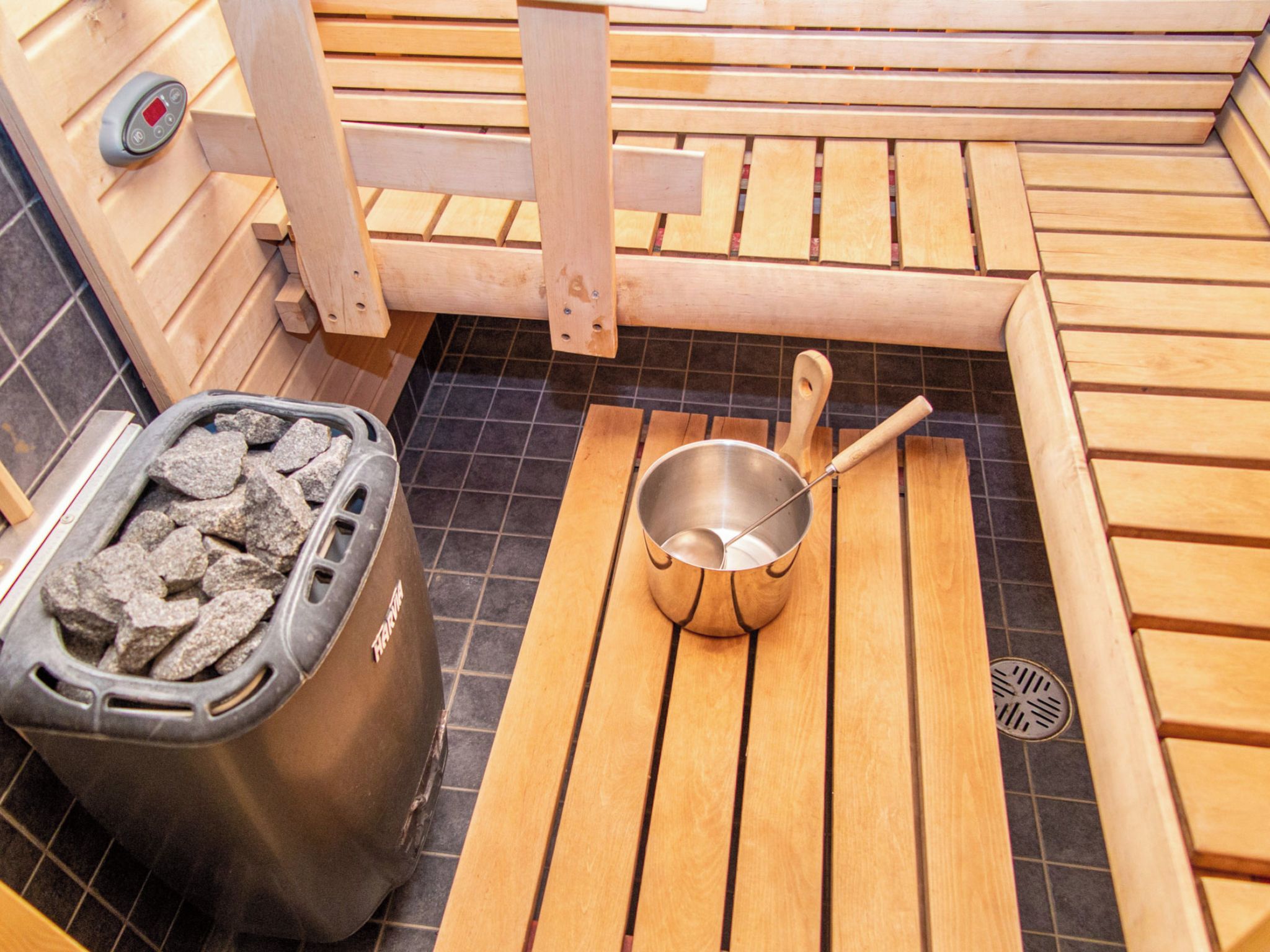 Una sauna amb bancs de fusta, un recipient metàl·lic amb pedres i una banyera metàl·lica amb una cullera.