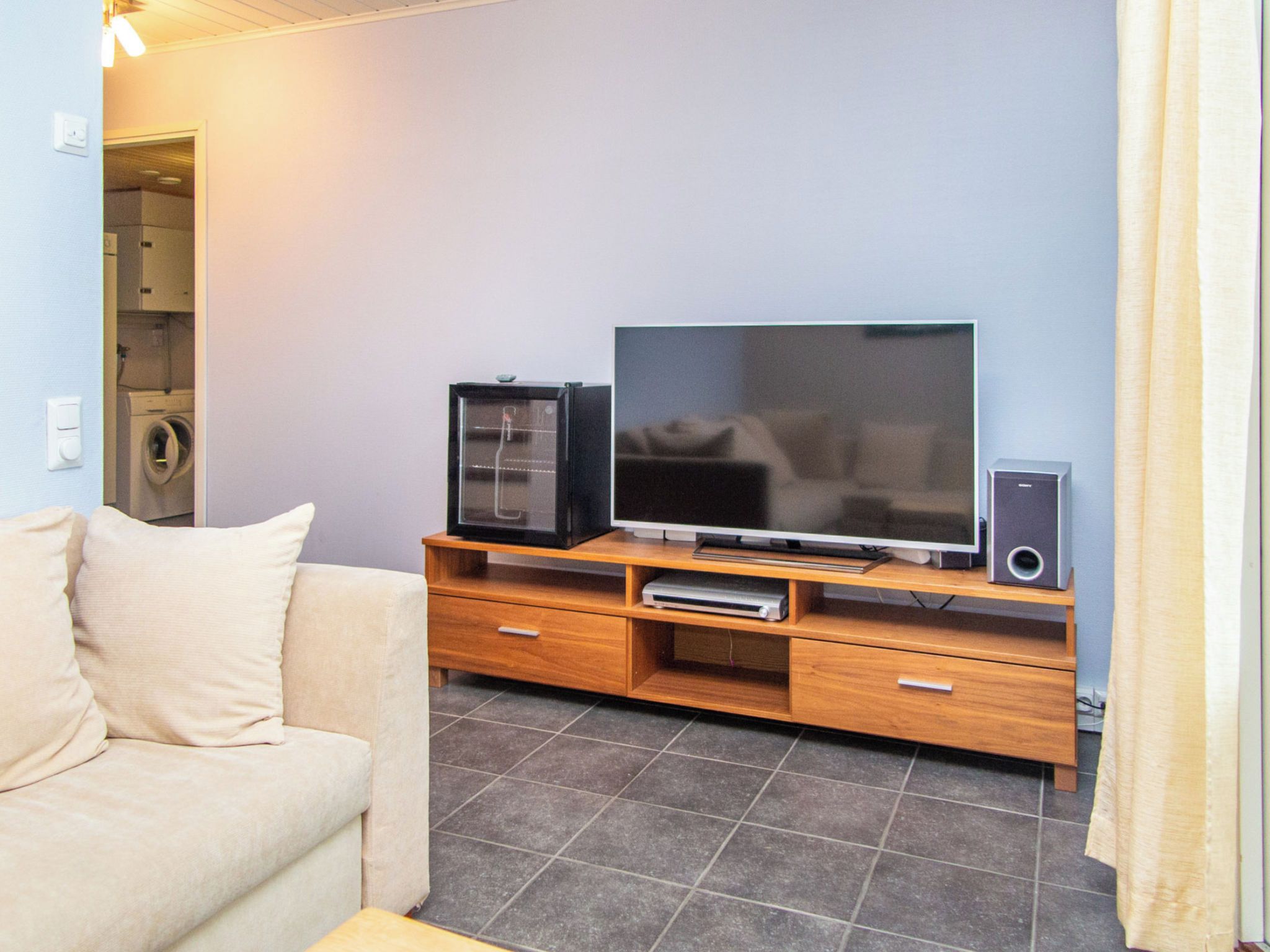 A living room with a sofa, a television, a DVD player, and a speaker on a wooden entertainment unit.