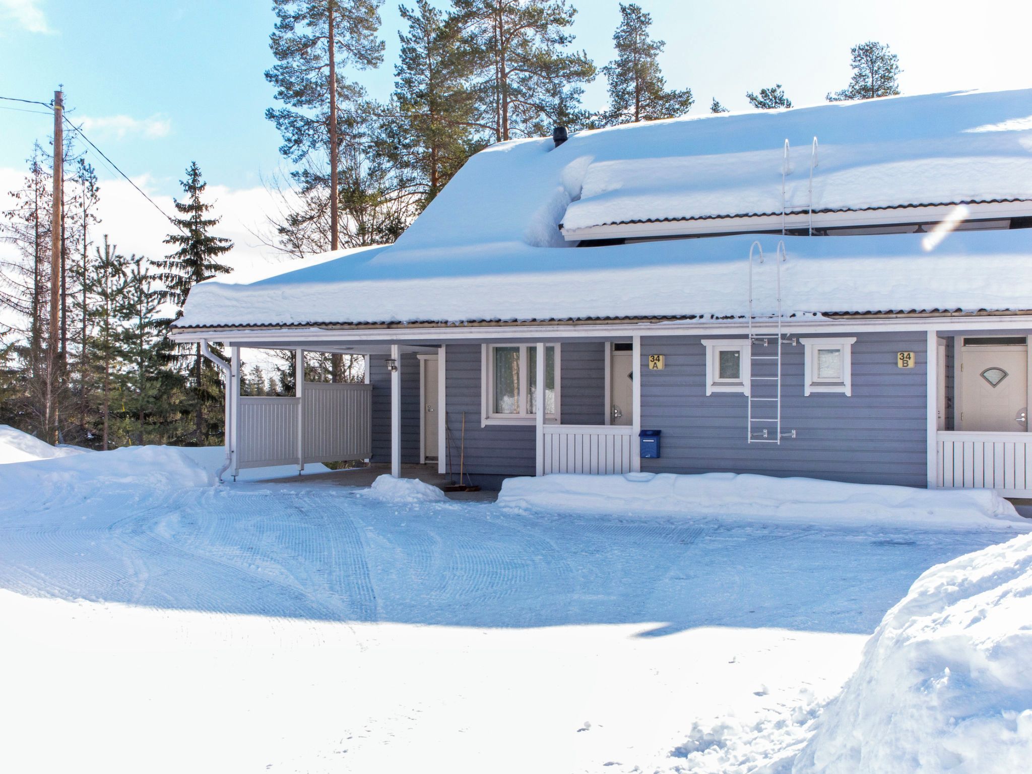 Ein zweistöckiges Haus mit einer Laube, einem mit Schnee bedeckten Dach und blauem Himmel.