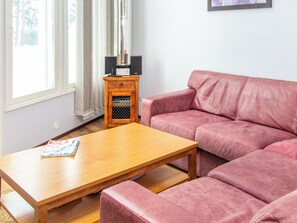 Un salon avec une table basse en bois, un canapé rose et un petit meuble en bois sur lequel se trouve un téléviseur.