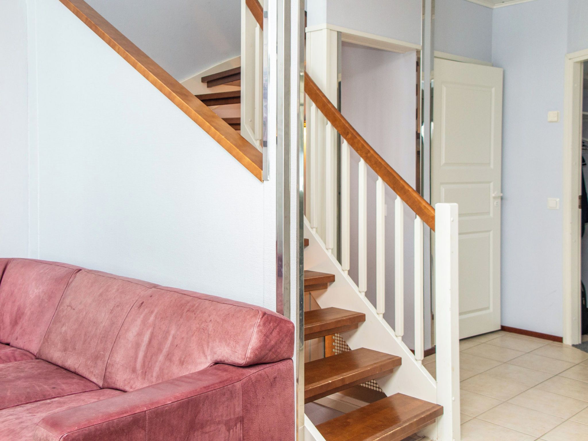 A staircase with wooden steps and white railings, a pink sofa, and a white door in a room with light-colored walls.
