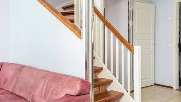 A staircase with wooden steps and white railings, a pink sofa, and a white door in a room with light-colored walls.