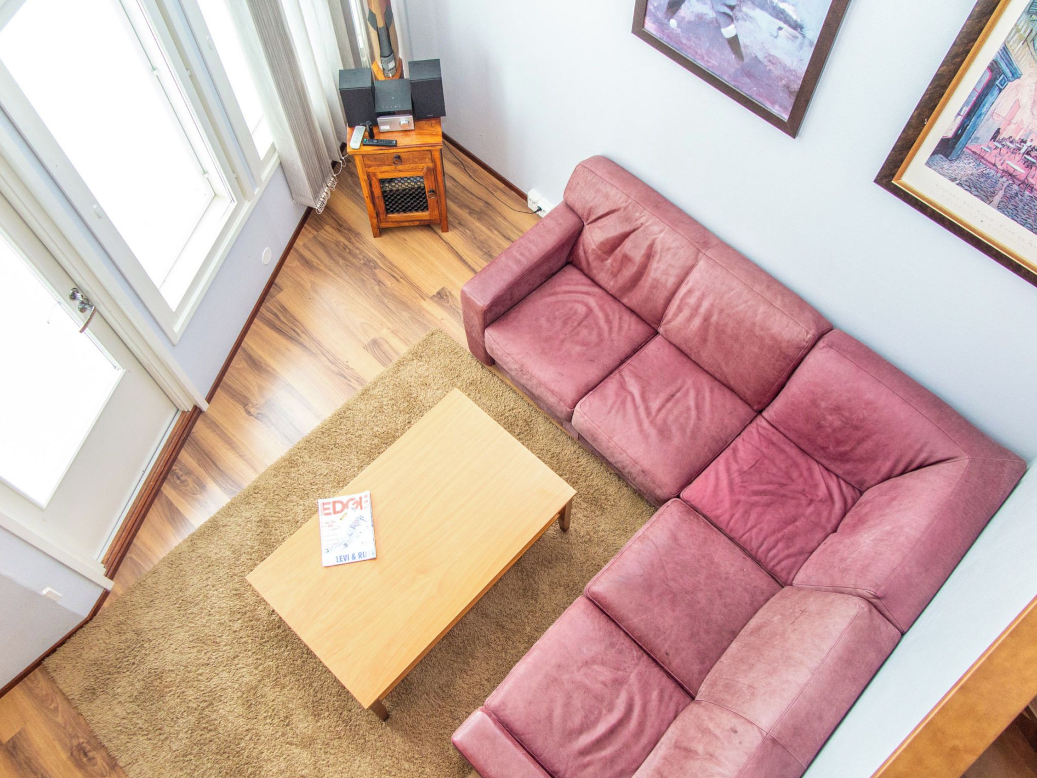 A living room with a wooden coffee table, a pink sofa, a small wooden side table with electronic devices, and a framed picture on the wall.