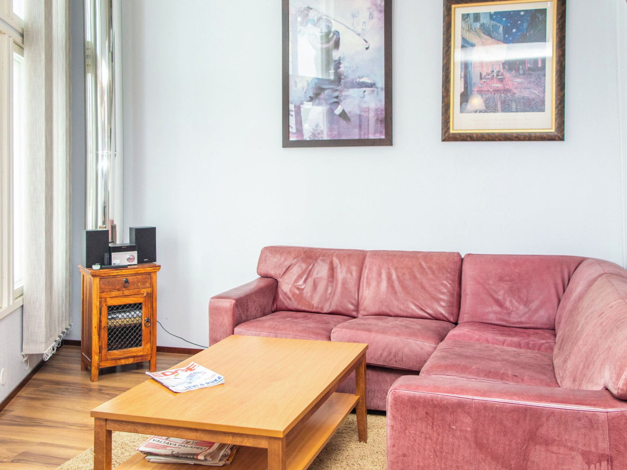 Ein Wohnzimmer mit einem Holztisch, einem rosafarbenen Sofa und einer kleinen Holzkommode mit einem Fernseher.