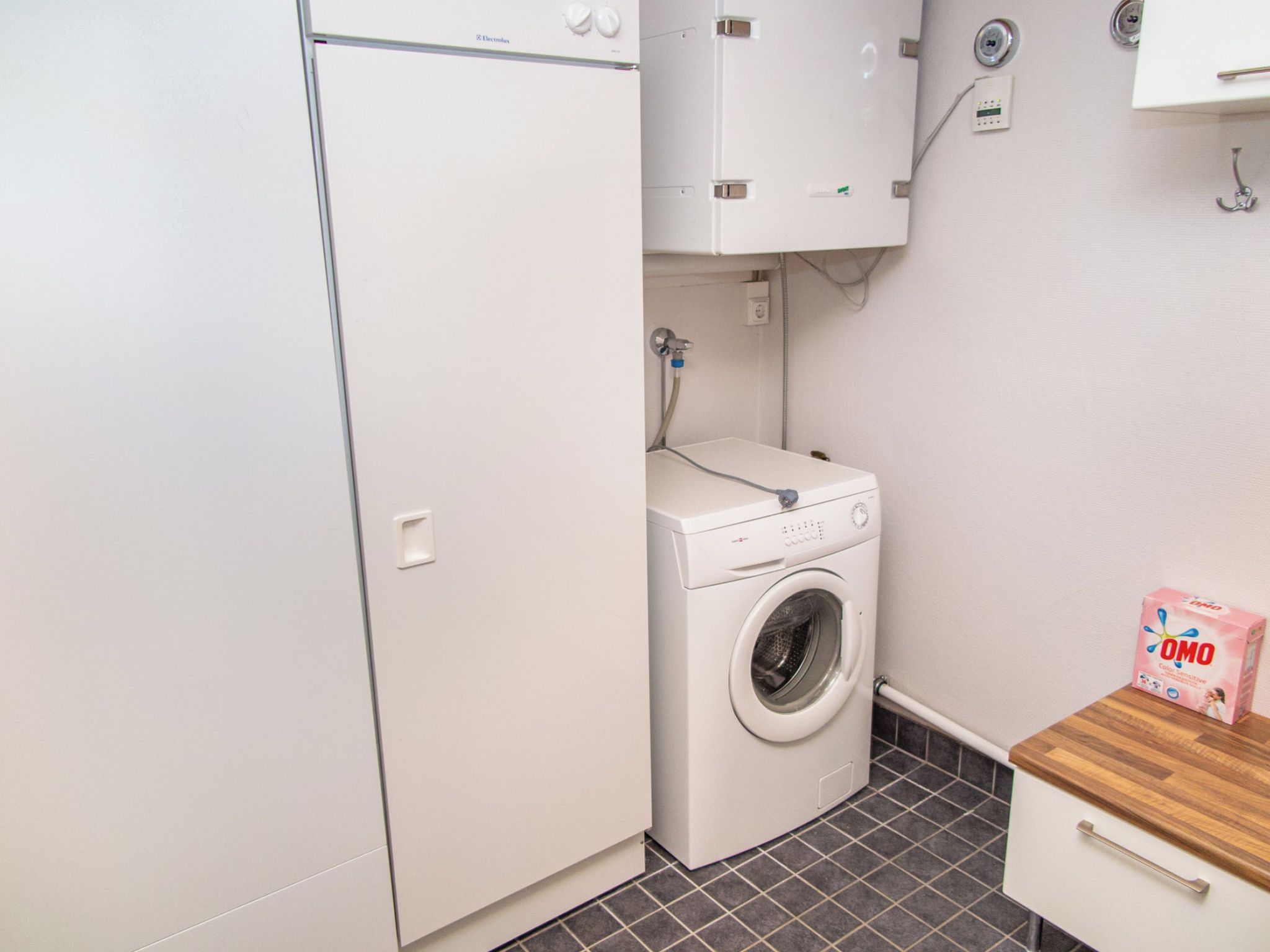 A compact laundry room with a washing machine, a dryer, and a small wooden table with a box of laundry detergent.