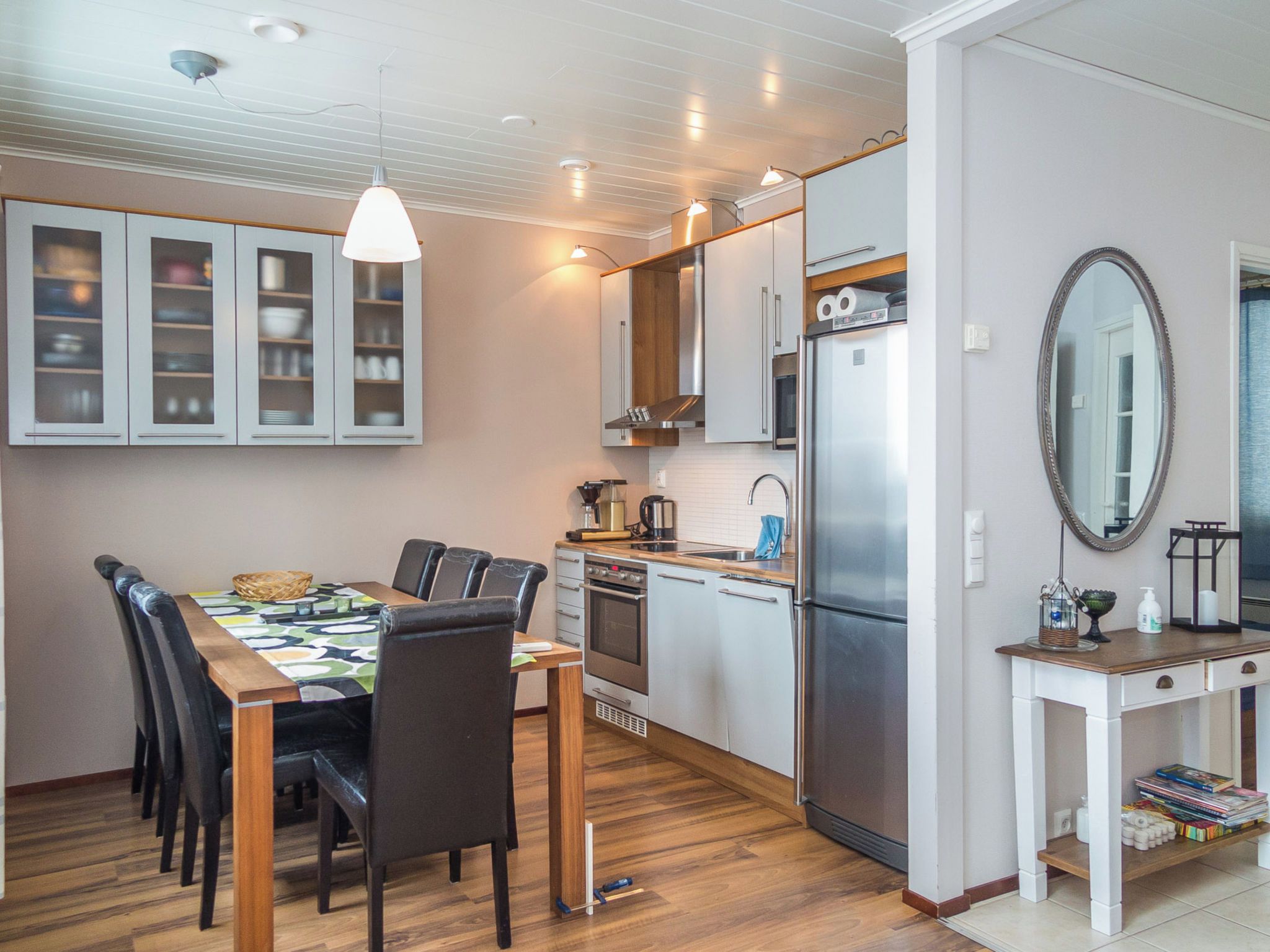 Una cucina compatta con elettrodomestici moderni, una zona pranzo con tavolo e sedie, e un piccolo tavolino con uno specchio e oggetti decorativi.