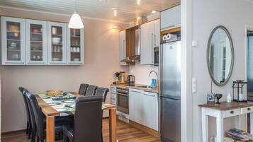 Cocina compacta con electrodomésticos modernos, comedor con mesa y sillas, y una mesita auxiliar con espejo y objetos decorativos.