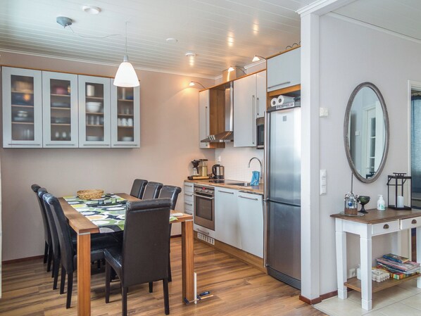 Cocina compacta con electrodomésticos modernos, comedor con mesa y sillas, y una mesita auxiliar con espejo y objetos decorativos.