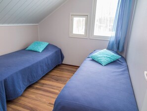 A room with two single beds, each with a blue bedspread and a matching pillow. The room has a sloped ceiling and a window with a view of trees. - Tahkonkallio 34 b by Interhome (Nilsiä)