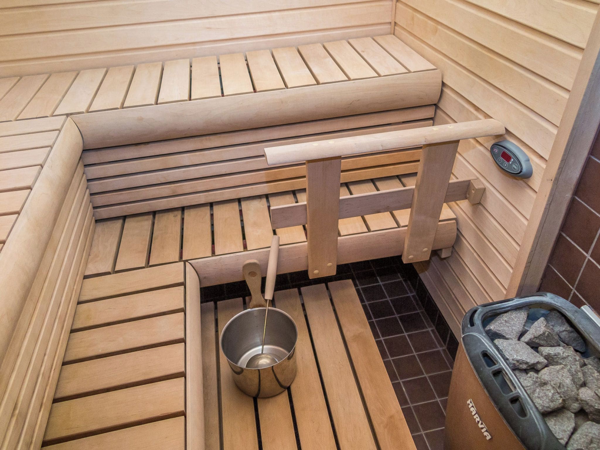 Een houten sauna met een metalen wasbak en bedieningspaneel.