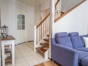 Een woonkamer met een blauwe bank, een houten trap en een witte deur.